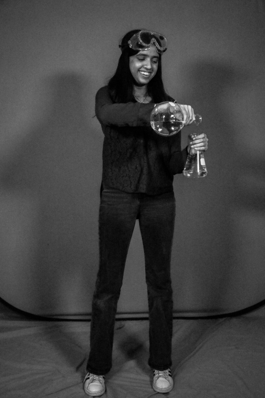 Shanza pouring between flasks, goggles on, in a studio portrait