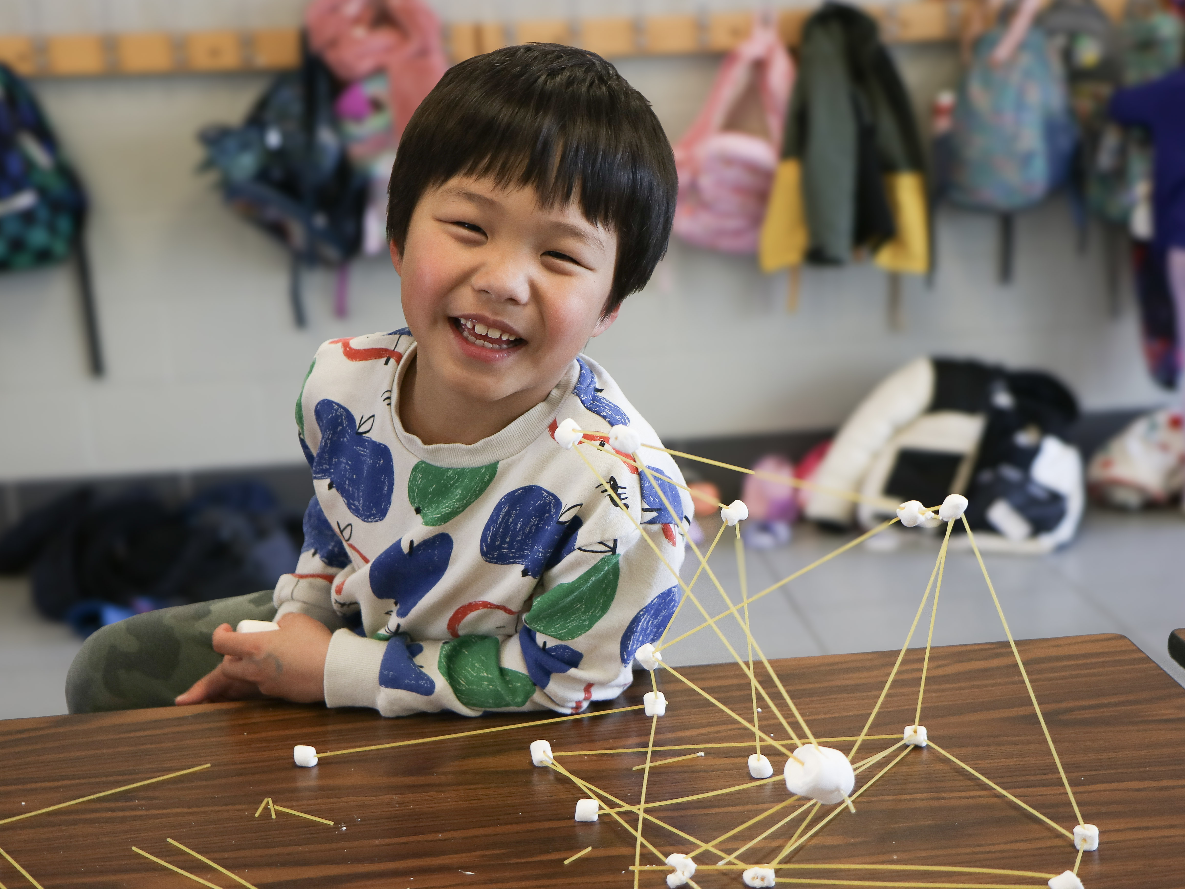 Young student smiling beside a spaghetti-and-marshmallow structure